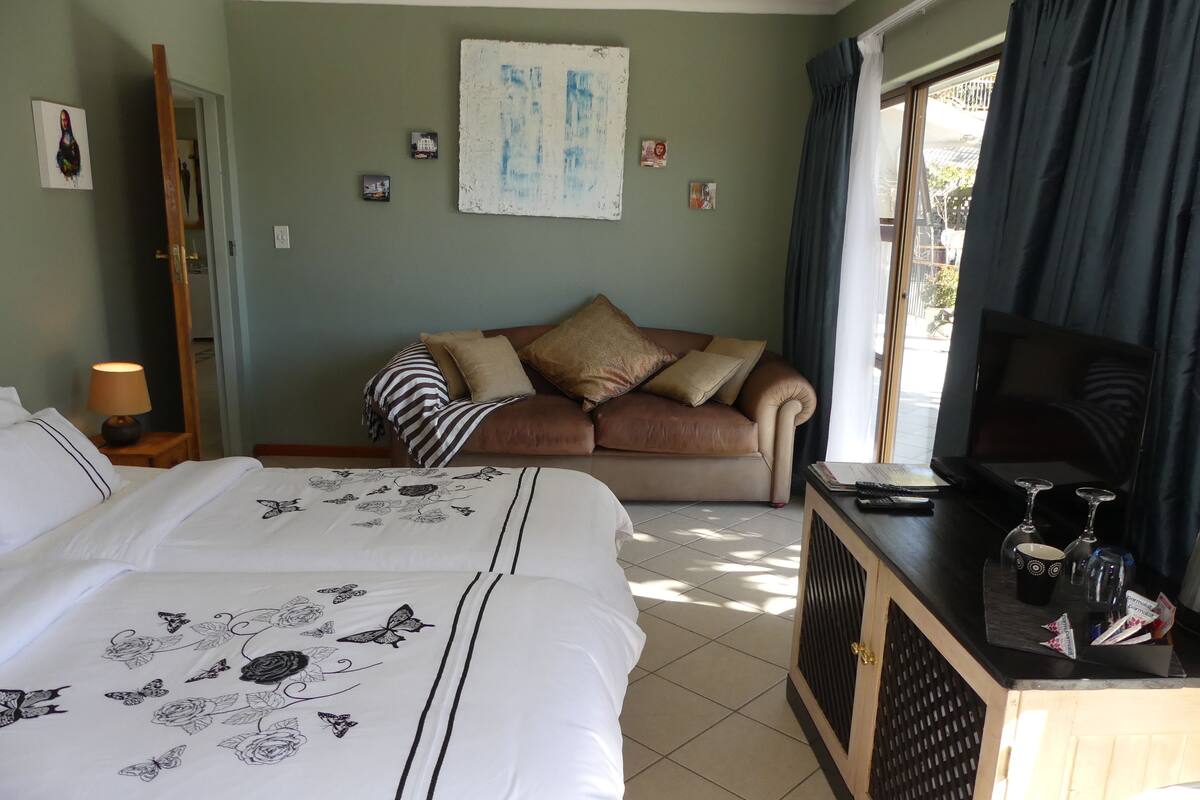 Ein Hotelzimmer mit Bett, einer Couch, einem Fernseher und einem Schreibtisch mit Weingläsern.