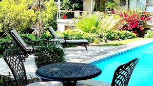 Un espace aménagé au bord de la piscine, avec une table ronde et deux chaises, entouré d’une végétation luxuriante et donnant sur la piscine.