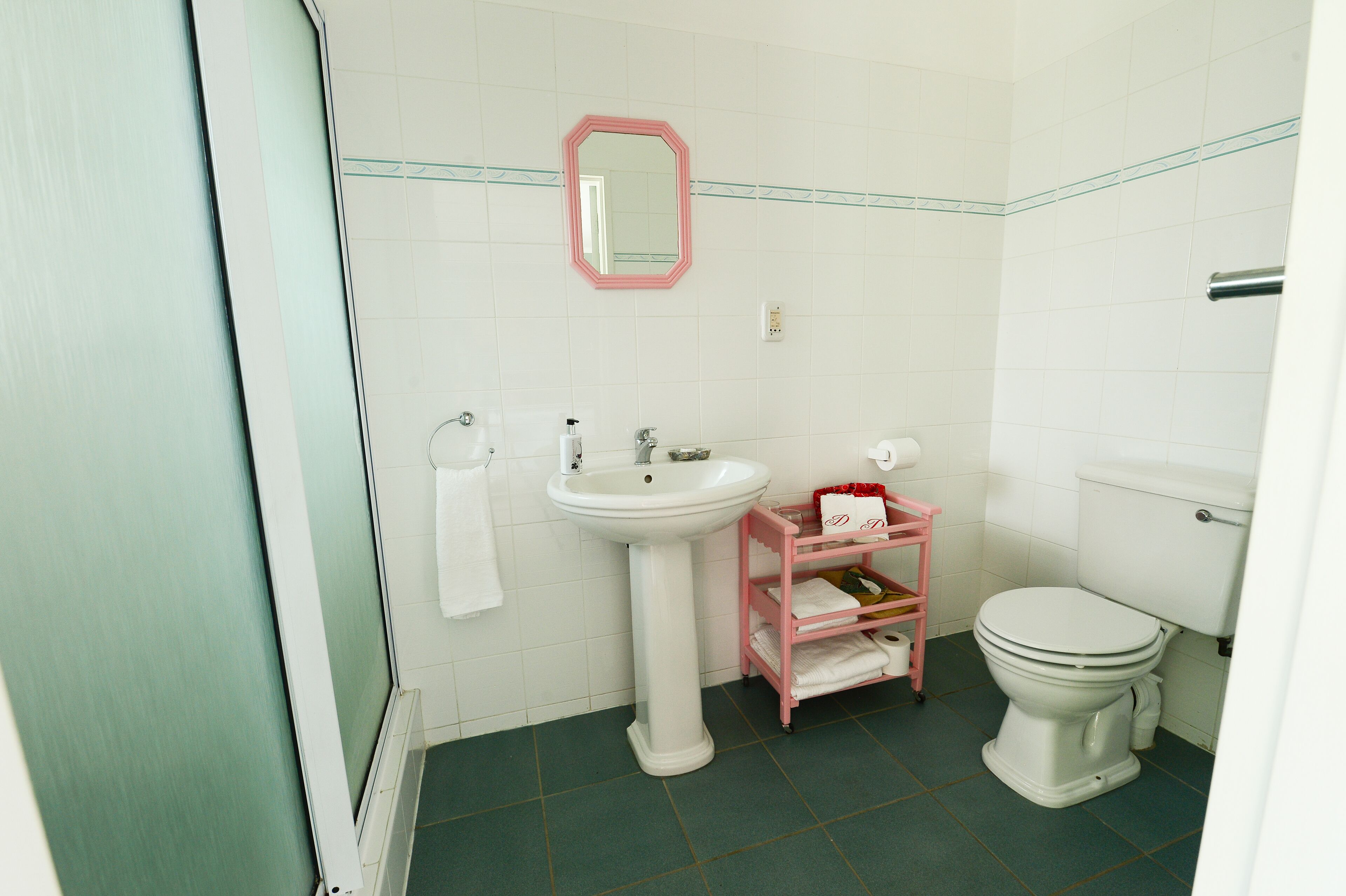 Un baño con lavamanos pedestal, inodoro y un mueble de almacenamiento rosa.