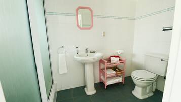 Un baño con lavamanos pedestal, inodoro y un mueble de almacenamiento rosa.