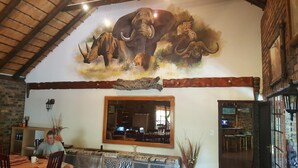 A restaurant with a large mural of wildlife, a rustic interior, and a dining area with a wooden table and chairs. - Jabula Lodge (Nkomazi)