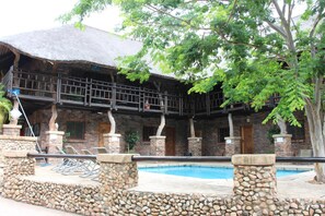 Un edificio con piscina, muros de piedra y techo de paja.