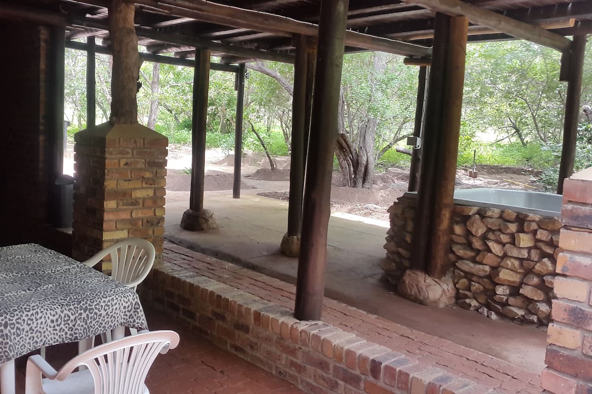 An outdoor patio with a table and chairs, a stone wall, and a view of trees.