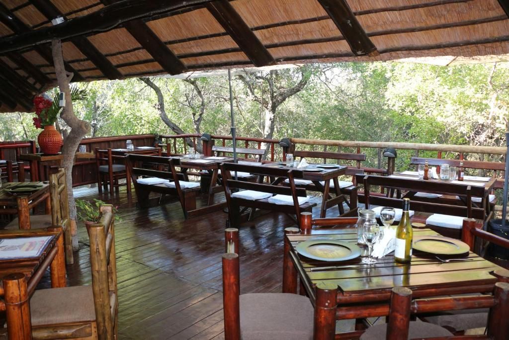 An outdoor dining area with wooden tables and benches, surrounded by trees.