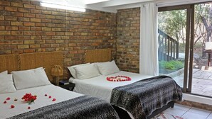 A hotel room with two beds, a brick wall, a large window, and a view of the outdoors. - Jabula Lodge (Nkomazi)