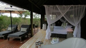 Ein Schlafzimmer mit Himmelsbett, einer Badewanne und zwei Liegestühlen unter einem Sonnenschirm.