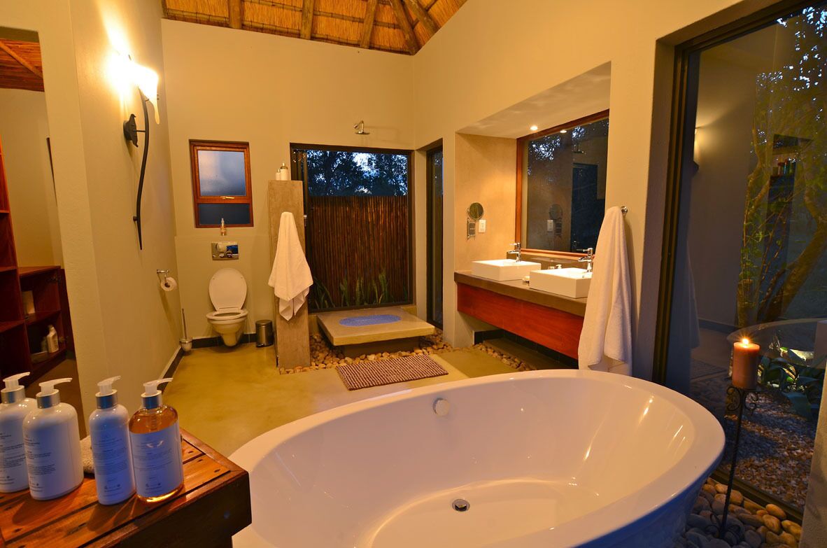 A modern bathroom with a large bathtub, a shower, and a vanity with a mirror. There are toiletries on a shelf and a candle on a table.
