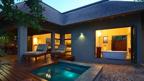 Ein modernes Haus mit Swimmingpool, Liegestühlen und einem durch die offene Tür einsehbaren Badezimmer.