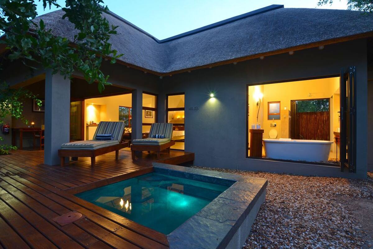 A modern house with a swimming pool, lounge chairs, and a bathroom visible through the open door.