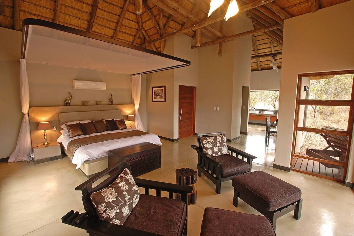 A spacious bedroom with a canopy bed, a sitting area with sofas, and a view of the outdoors.