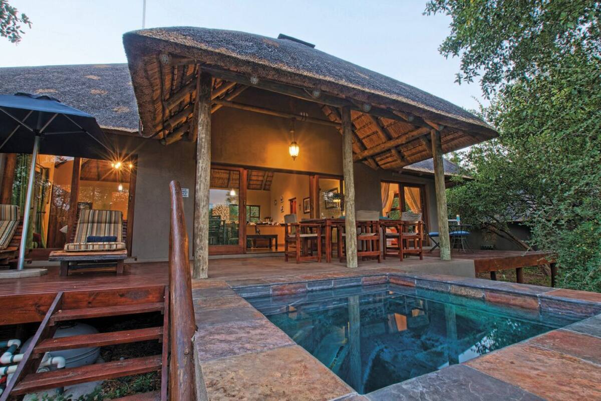 A poolside area with a thatched roof, wooden deck, and a clear pool.