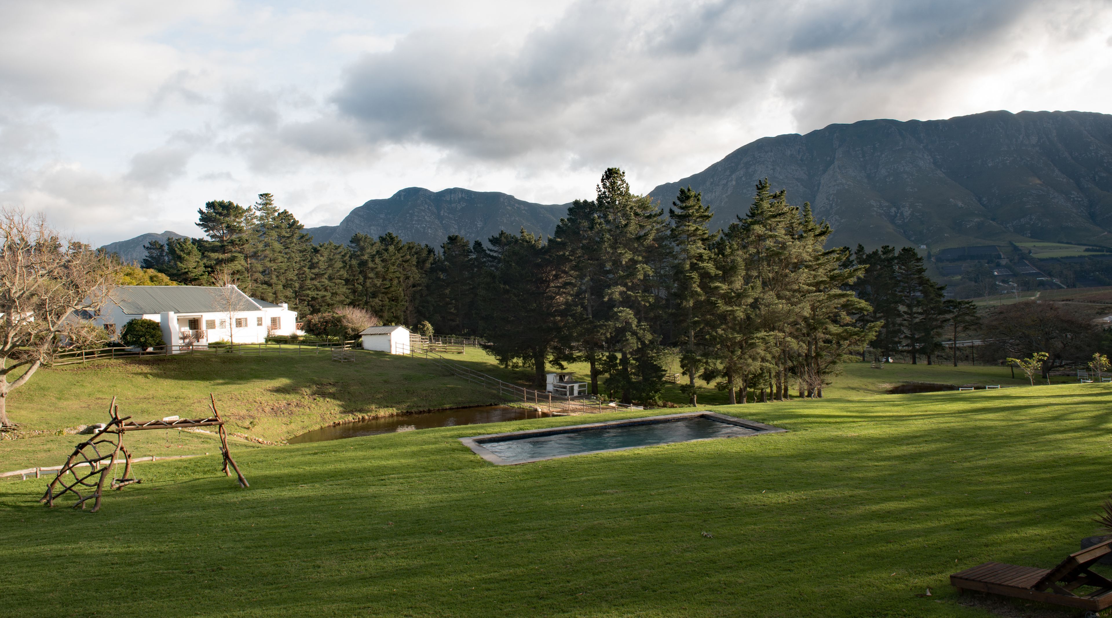 A white house with a fenced yard, a small pond, and a mountainous backdrop.