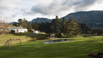 A white house with a fenced yard, a small pond, and a mountainous backdrop.