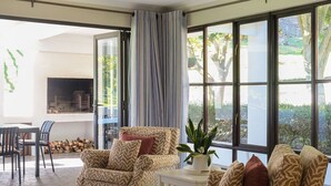 A spacious living area with a sofa set, a dining table, and chairs. There is a large window with a view of the outdoors, and a fireplace is visible through the glass doors. - High Season Farm (Hermanus)