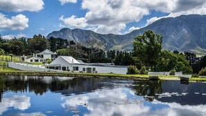 A lakeside property with a white building, a pond, and mountains in the background. - High Season Farm (Hermanus)