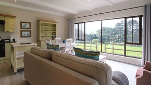 A spacious living room with a large window, a ceiling fan, and a dining area with a table and chairs. - High Season Farm (Hermanus)
