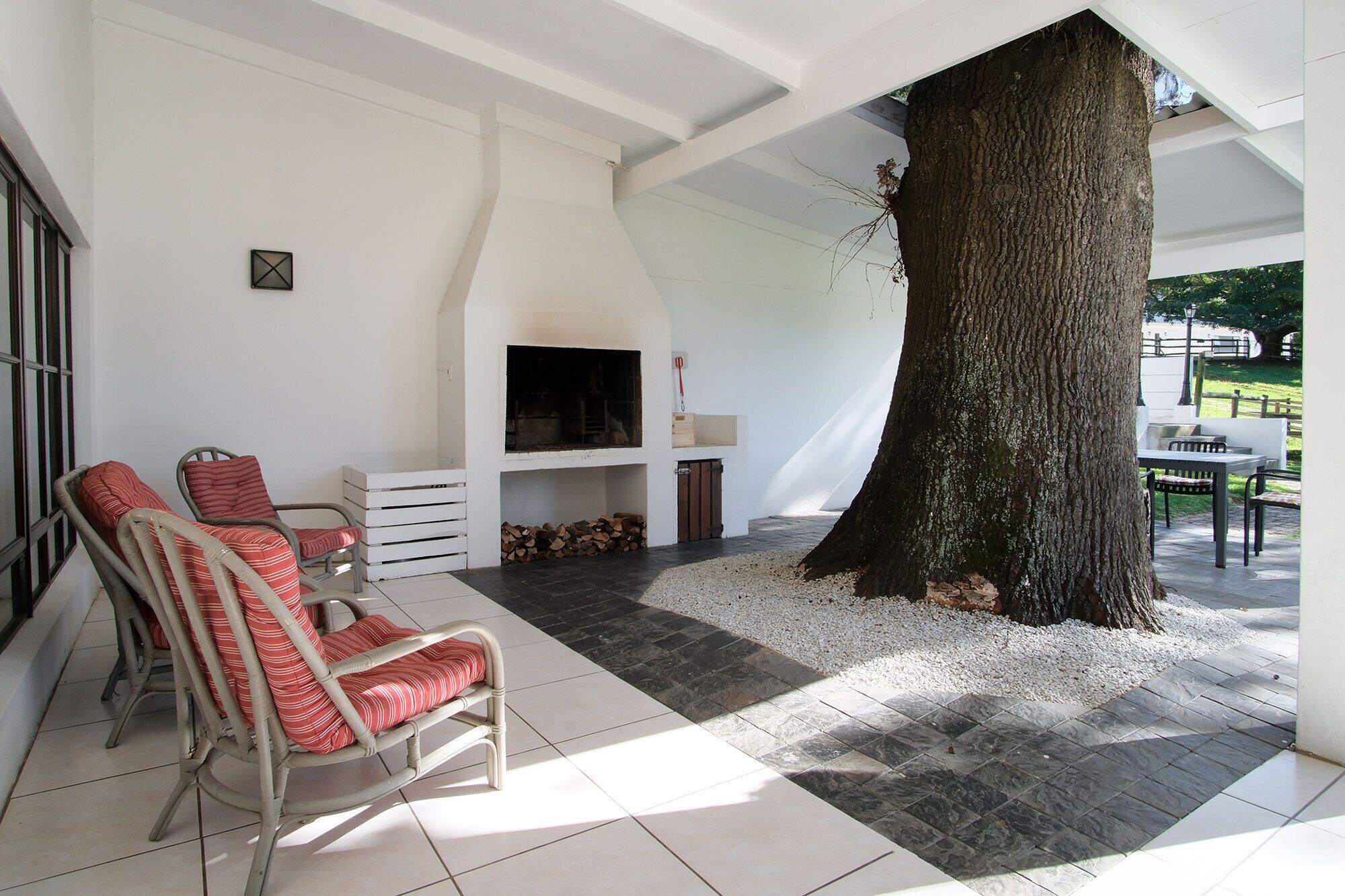 A spacious living area with a fireplace, wicker chairs, and a large tree.
