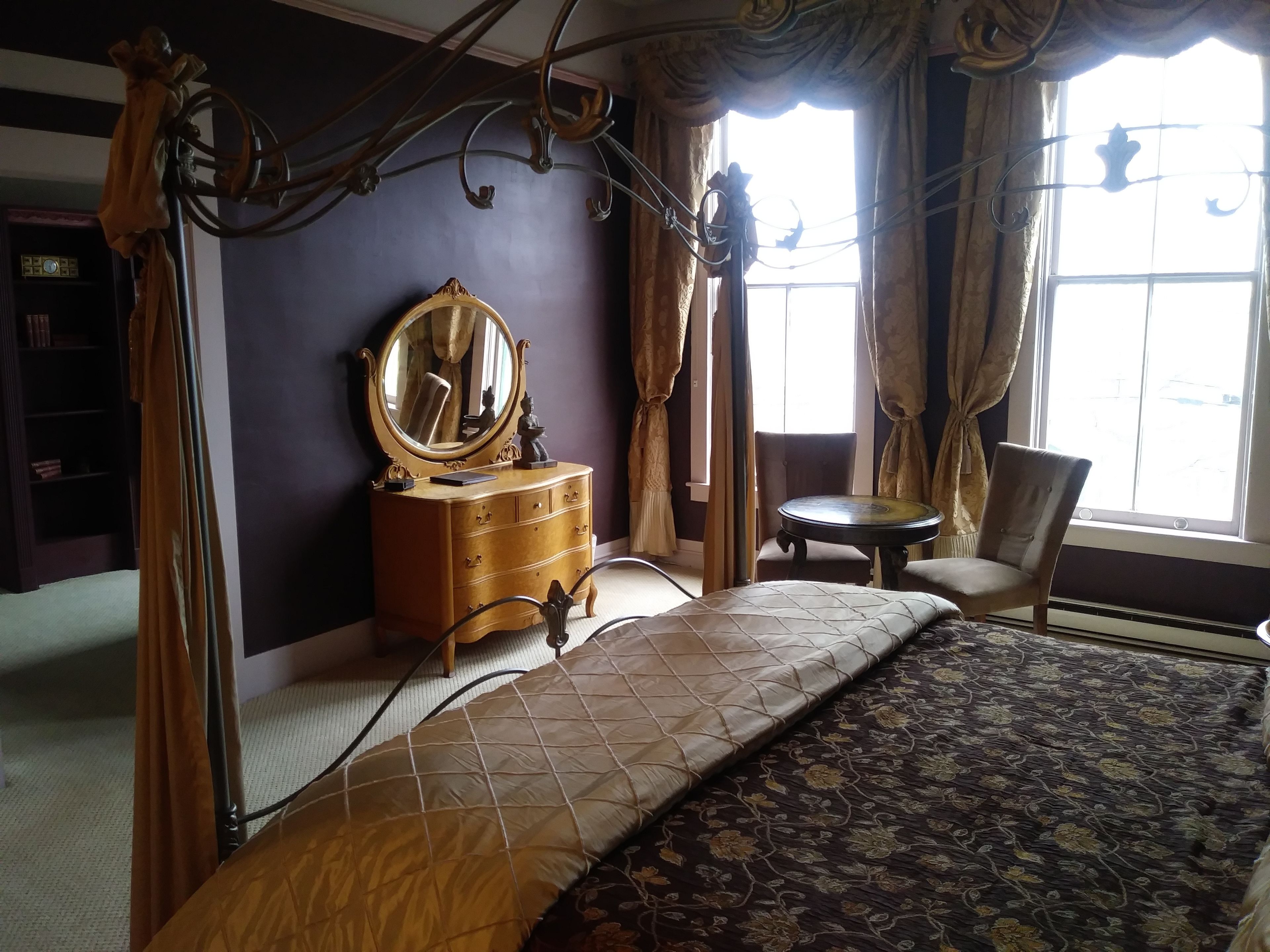 A bedroom with a bed, a dresser with a mirror, a chair, and a window with curtains.