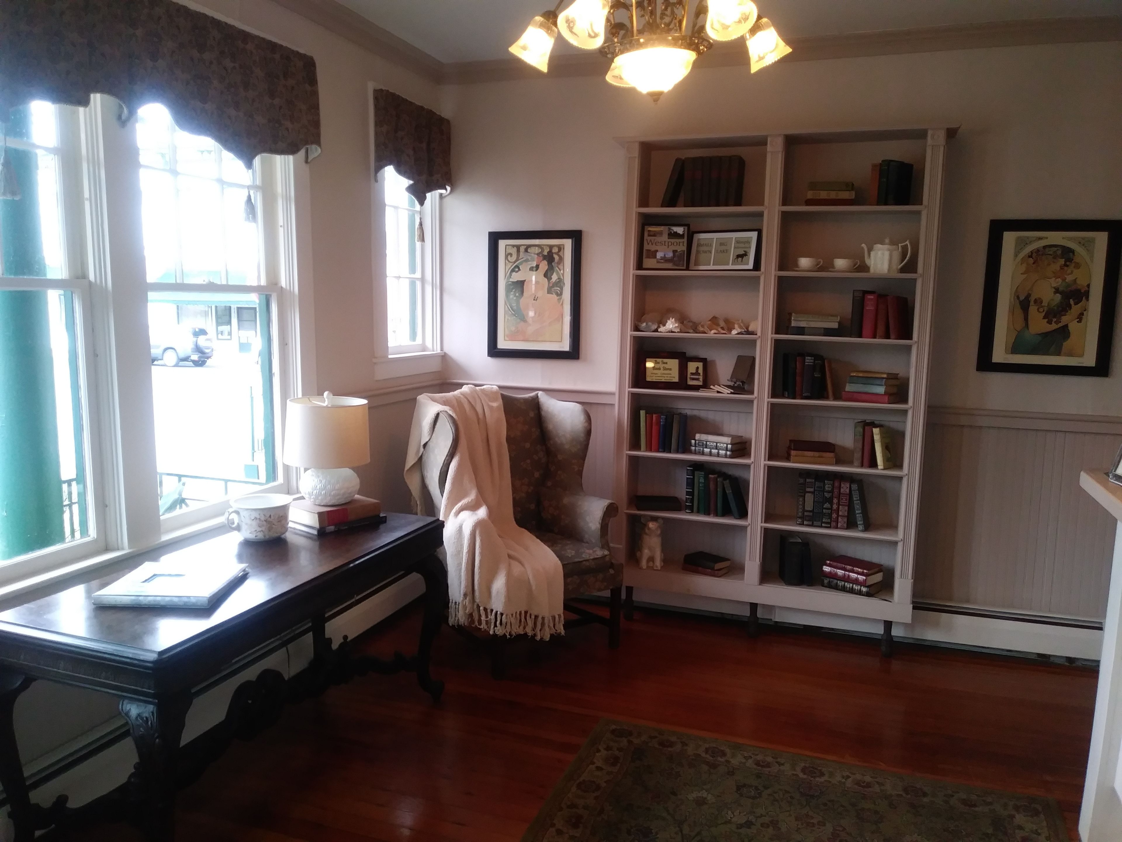 A cozy reading nook with a chair, a bookshelf, and a desk with a lamp.