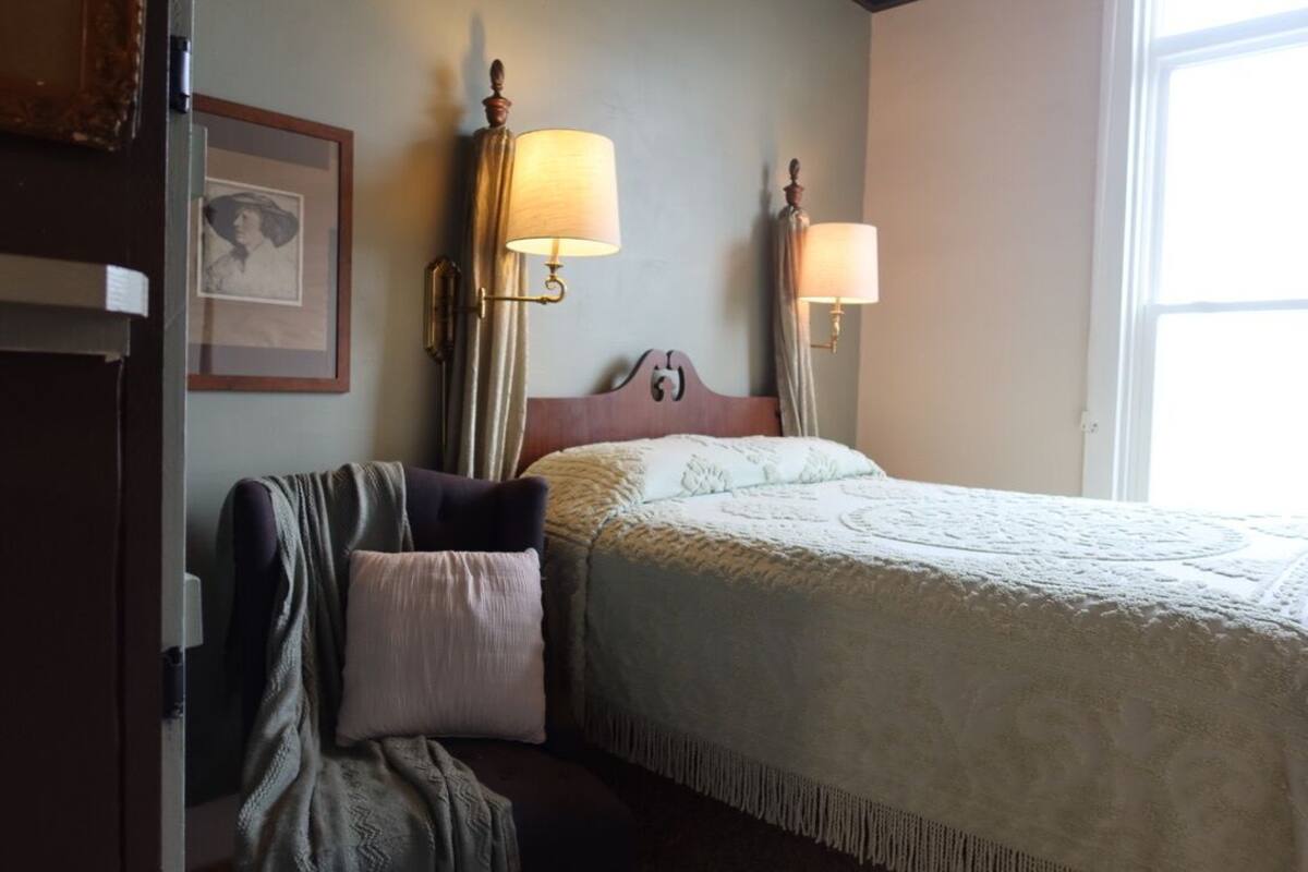 A hotel room with a bed, a chair, a lamp, and a framed picture on the wall.
