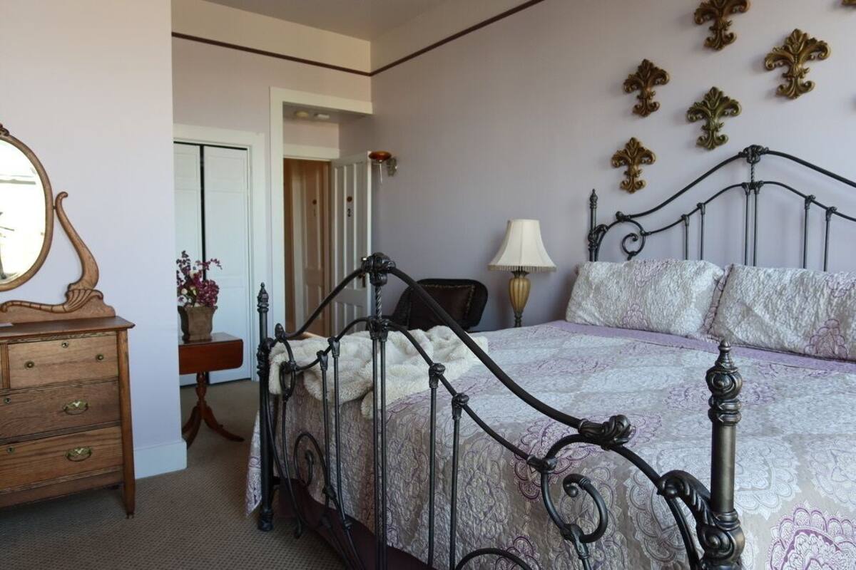 A bedroom with a four-poster bed, a wooden dresser, a mirror, and decorative wall pieces.