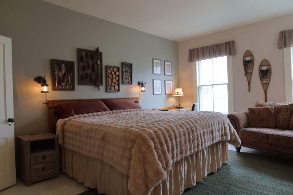 A bedroom with a large bed, bedside tables, a sofa, wall-mounted lamps, and framed pictures.