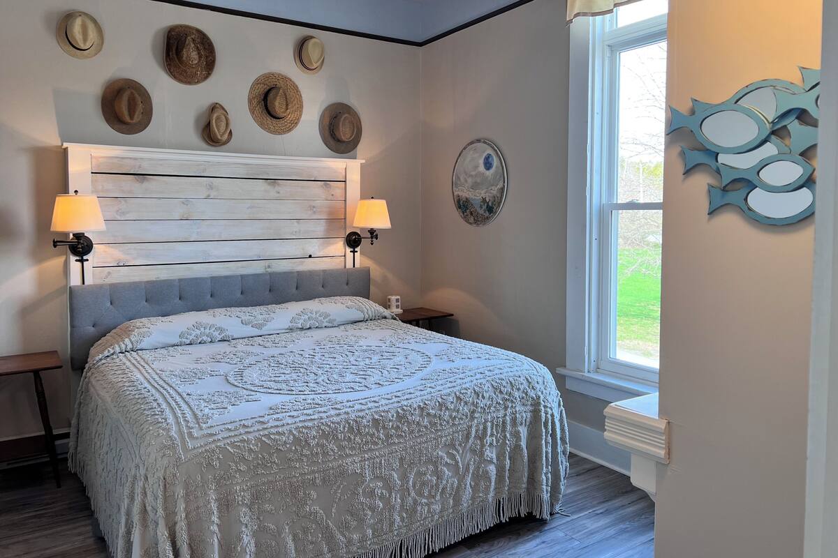 A bedroom with a wooden headboard, a bed with a white patterned bedspread, wall-mounted lamps, and decorative wall art.