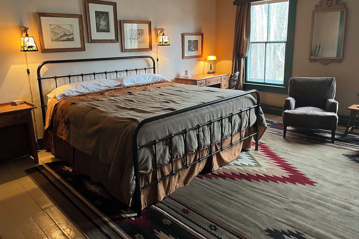 A bedroom with a bed, a chair, a window, and framed pictures on the wall.