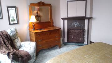 A bedroom with a bed, a dresser, a mirror, a lamp, a fireplace, and a patterned armchair.