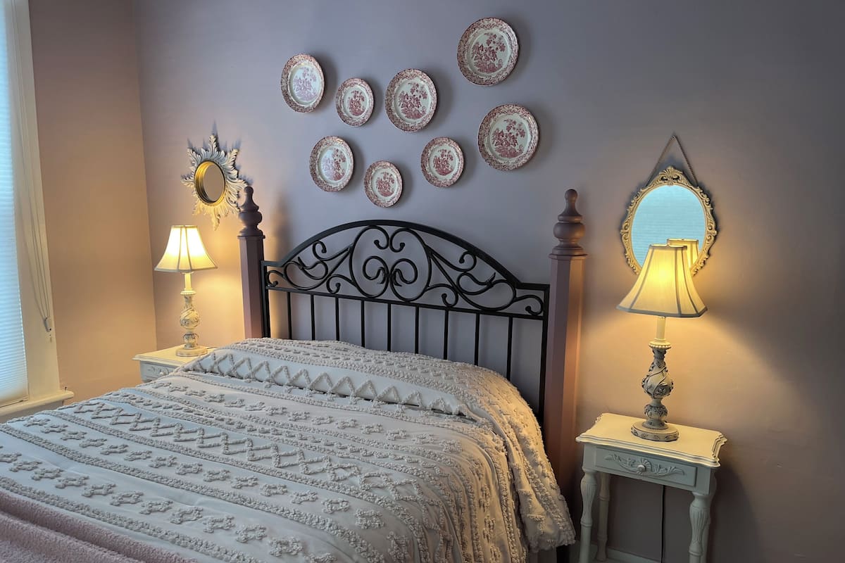 A bedroom with a bed, two bedside tables, a wall-mounted mirror, and a series of decorative plates.