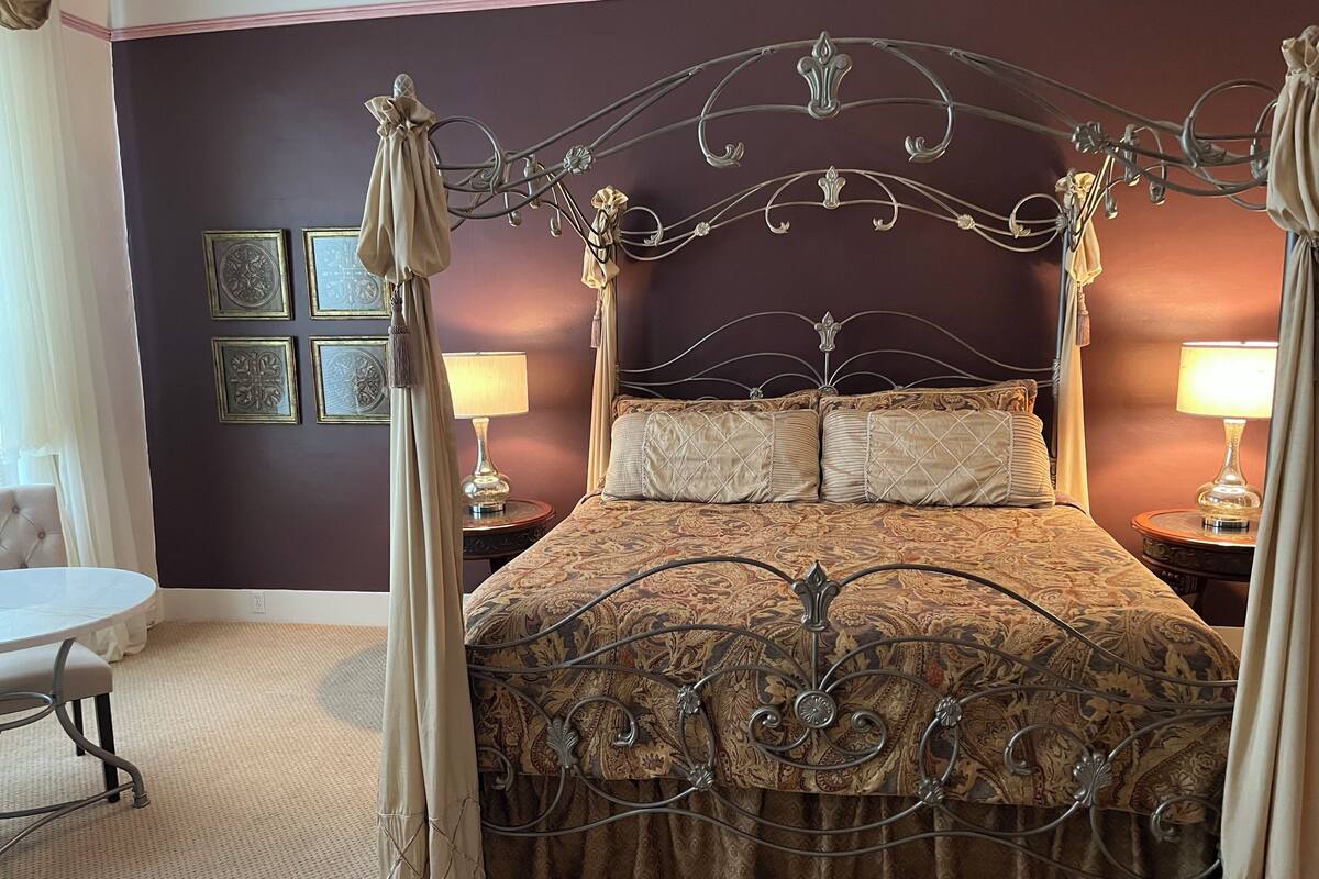 A four-poster bed with a metal frame, two bedside tables with lamps, and a chair.