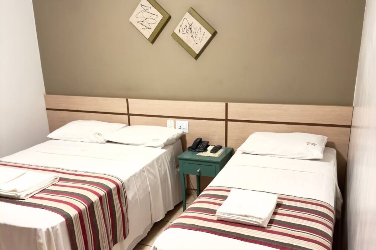 Habitación de hotel con dos camas individuales, una mesita con un teléfono y un interruptor de luz en la pared.