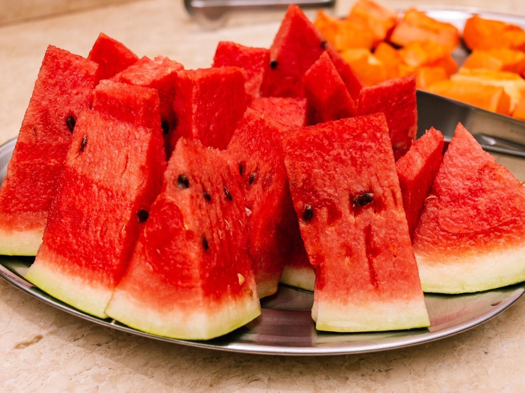 A plate of watermelon slices with a few orange fruits in the background.