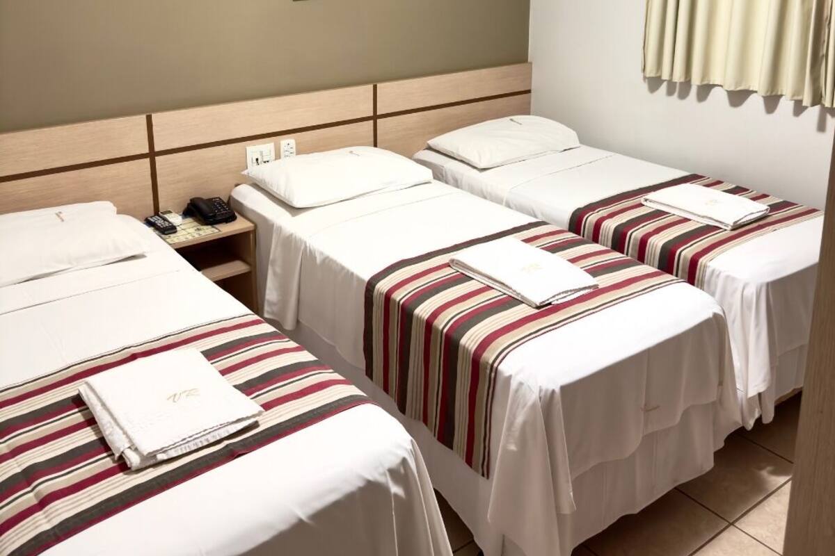 Habitación de hotel con dos camas individuales, una mesita de noche con teléfono y aire acondicionado de pared.