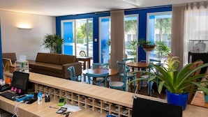A hotel lobby with a reception desk, seating area, and large windows offering views of the street. - Hotel Villa Rebellato (Olímpia)