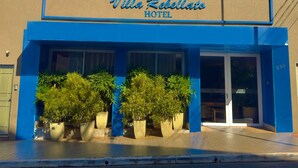 The exterior of Villa Rebello Hotel with a blue facade, large potted plants in front, and a clear entrance. - Hotel Villa Rebellato (Olímpia)
