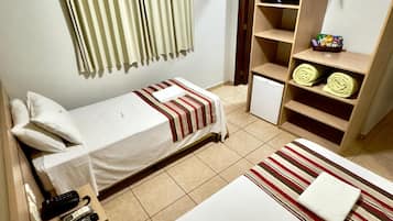 Habitación de hotel con dos camas individuales, un armario, un pequeño escritorio con teléfono y un estante con toallas dobladas.