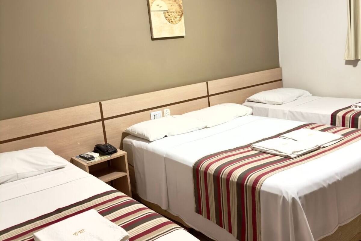 Habitación de hotel con dos camas, una mesita de noche con teléfono y una obra de arte colgada en la pared.