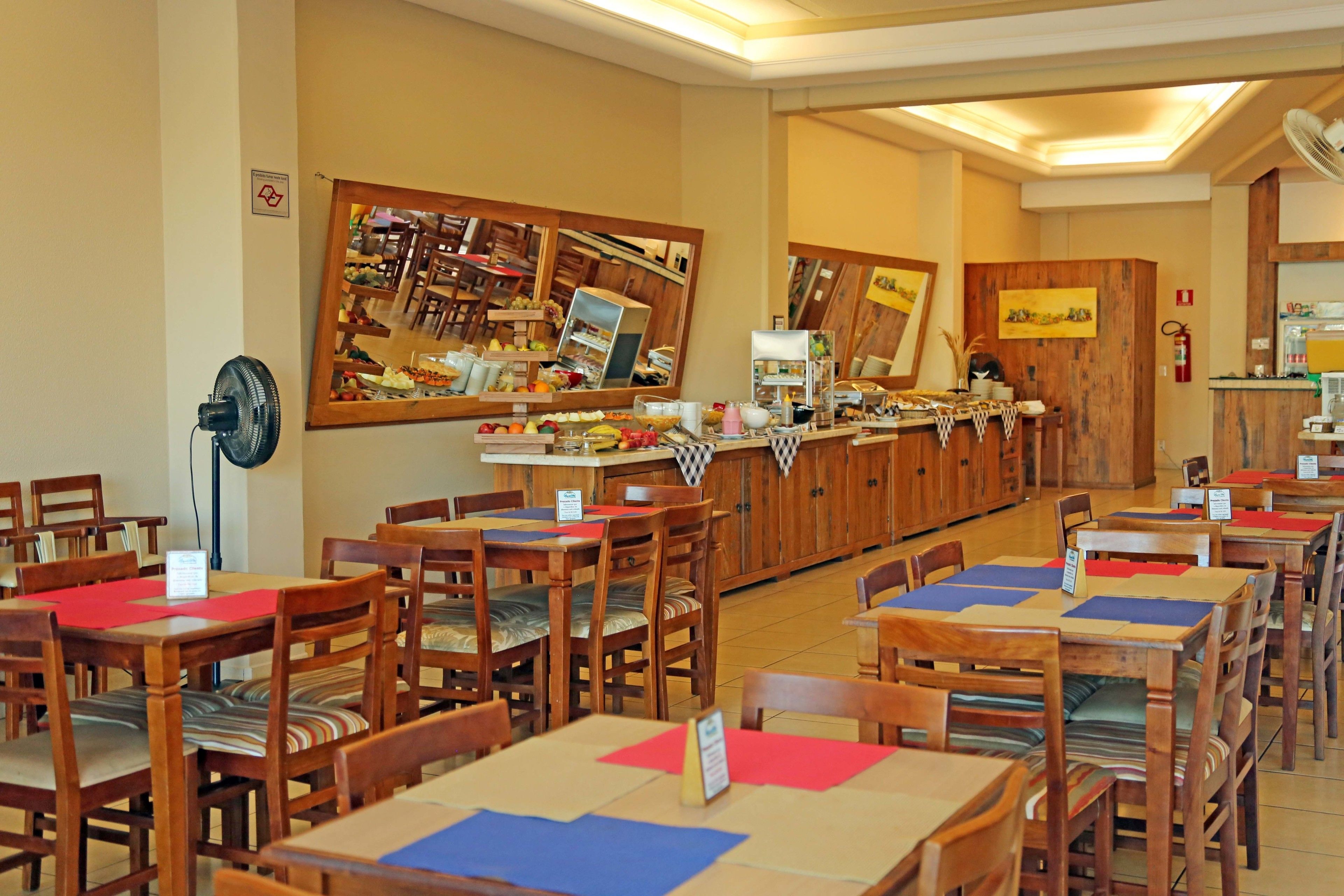 Un restaurante con mesas y sillas de madera, una barra con productos alimenticios y un espejo que refleja el interior.