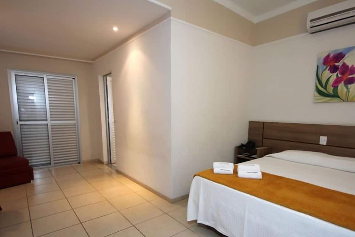 A hotel room with a bed, a nightstand, a chair, and a sliding door.