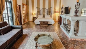 A bedroom with a large bed, a chandelier, a fireplace, and a view of the outdoors. - Casa Liza (San Miguel de Allende)