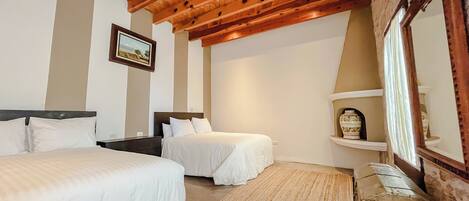 A bedroom with two beds, a wooden ceiling, a painting, a mirror, and a small shelf with decorative items.