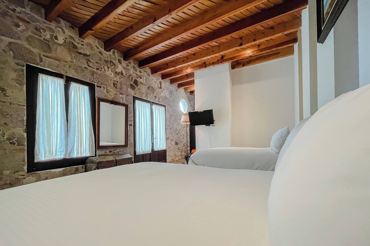 Une chambre avec un mur en pierre, des poutres en bois, un lit, une télévision et un miroir.