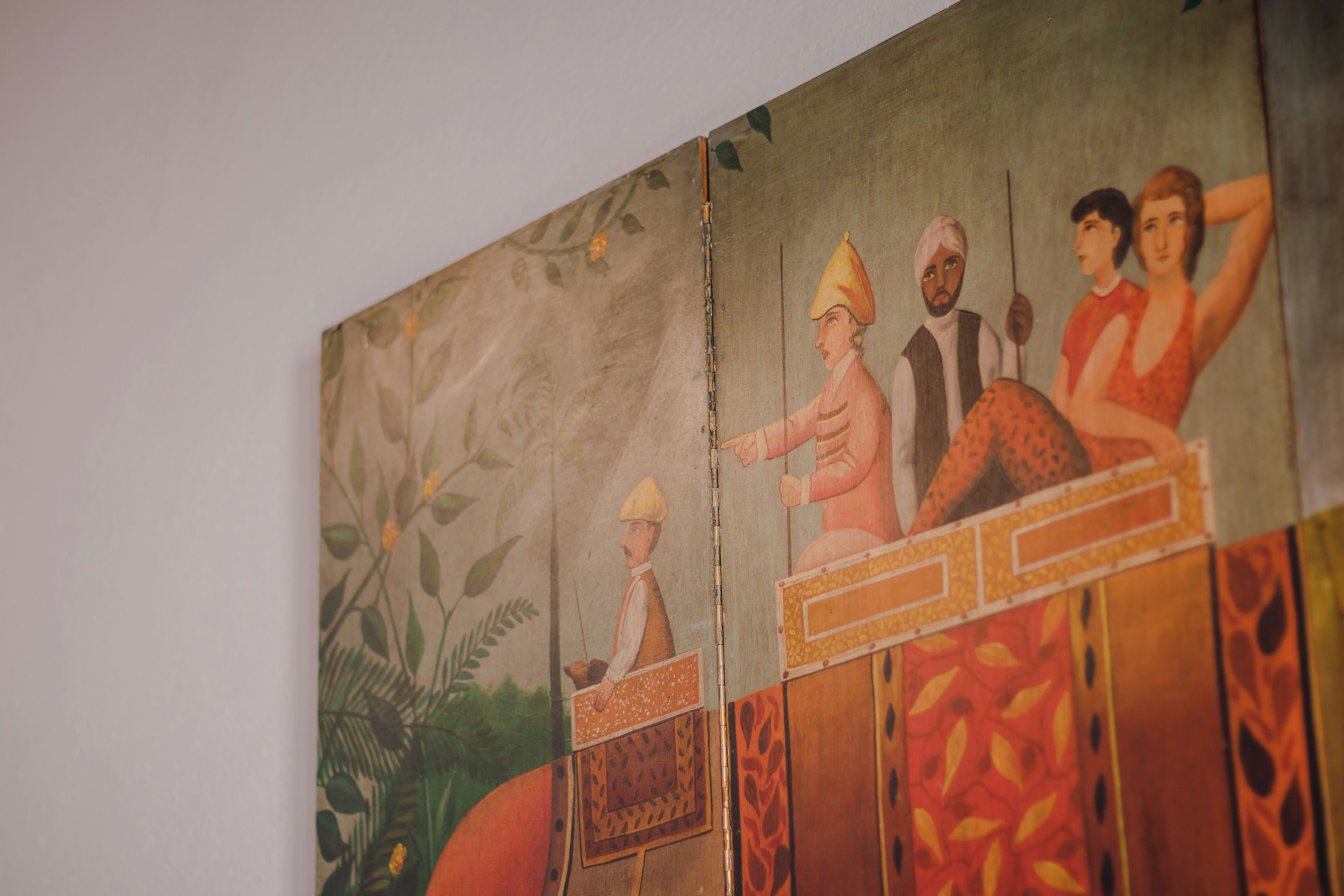 Un mur orné d’un tableau représentant une scène avec des personnes et des plantes.