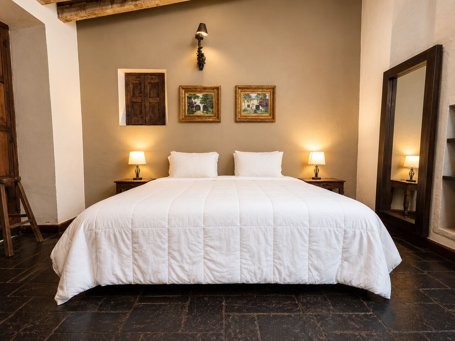 Une chambre d’hôtel avec un grand lit, deux tables de chevet avec des lampes, une porte en bois et deux tableaux encadrés au mur.