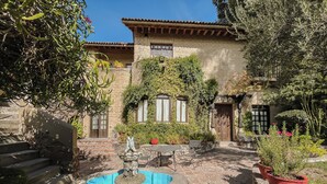 A courtyard with a fountain, stone steps, potted plants, and a building with a tiled roof and stone walls. - Casa Liza (San Miguel de Allende)