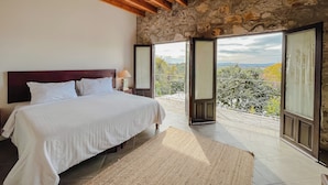 A bedroom with a stone wall, wooden ceiling beams, a bed with white bedding, and a view through an open door to a balcony. - Casa Liza (San Miguel de Allende)