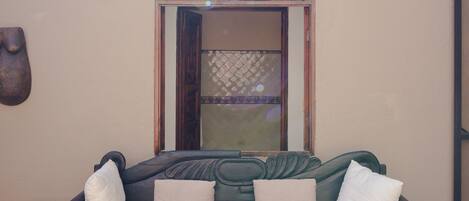 A dark green sofa with white cushions in a room with a tiled floor and a decorative wall piece.