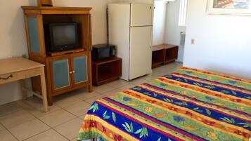 A bedroom with a bed, a television, a microwave, and a refrigerator.