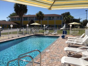 A swimming pool with a brick deck, white lounge chairs, and umbrellas. - Economy Suites (Winter Haven)